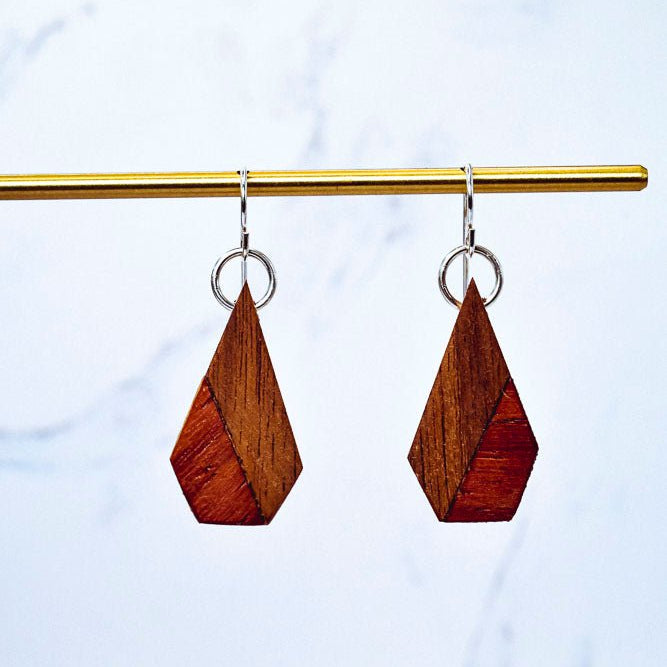 Wooden teardrop earrings hanging from a gold rod against a light blue background