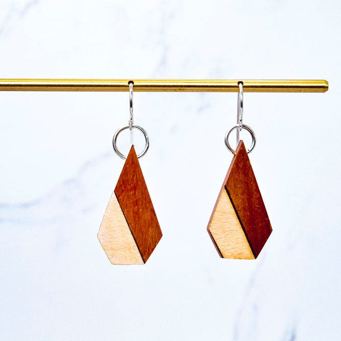 Wooden geometric earrings on a gold rod against a light blue background