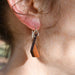 Close-up of an earring with a wooden pendant worn by a person outdoors.