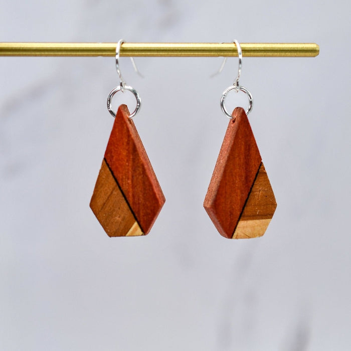Wooden geometric earrings on a gold rod against a light gray background