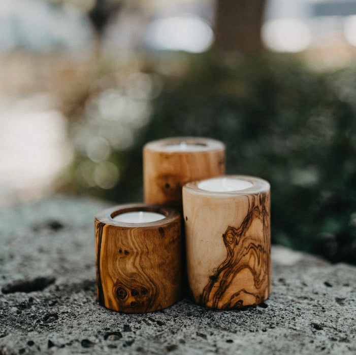 Three wooden candle holders on a stone surface with a blurred natural background