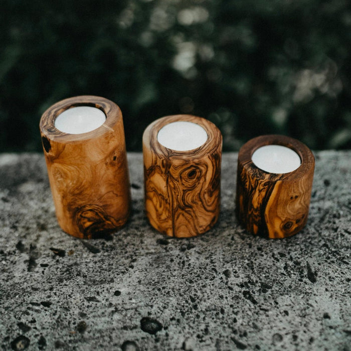 Three wooden candle holders with candles on a stone surface with a blurred natural background