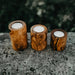 Three wooden candle holders with candles on a stone surface with a blurred natural background