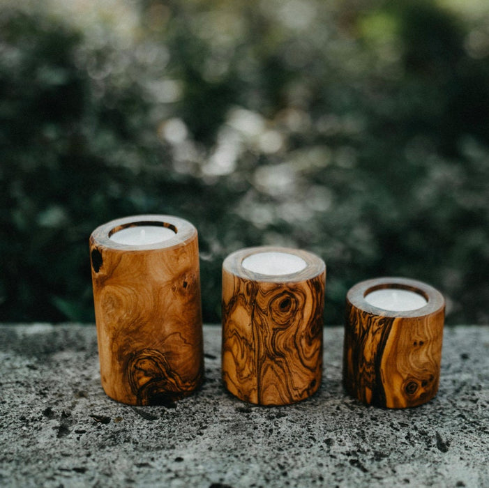 Three wooden candle holders with candles on a stone surface with a blurred natural background
