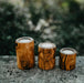 Three wooden candle holders with candles on a stone surface with a blurred natural background