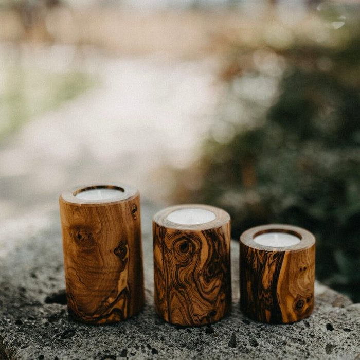 Three wooden candle holders on a stone surface with a blurred natural background