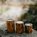 Three wooden candle holders on a stone surface with a blurred natural background