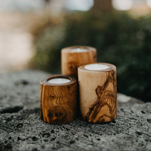 Three wooden candle holders with candles on a stone surface outdoors.