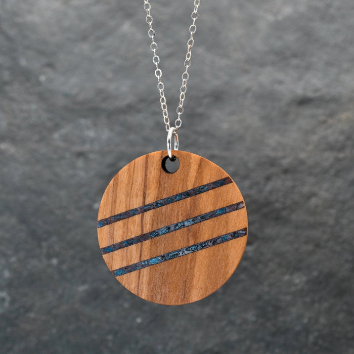 Wooden pendant with black stripes on a chain against a dark gray background