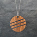 Wooden pendant with black stripes on a chain against a dark gray background
