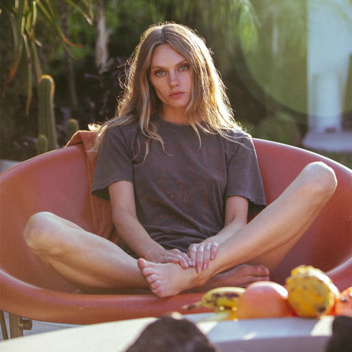 Woman sitting in a pink chair outdoors with greenery in the background