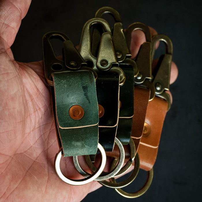 Hand holding three leather keychains with metal rings against a dark background