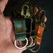 Hand holding three leather keychains with metal rings against a dark background